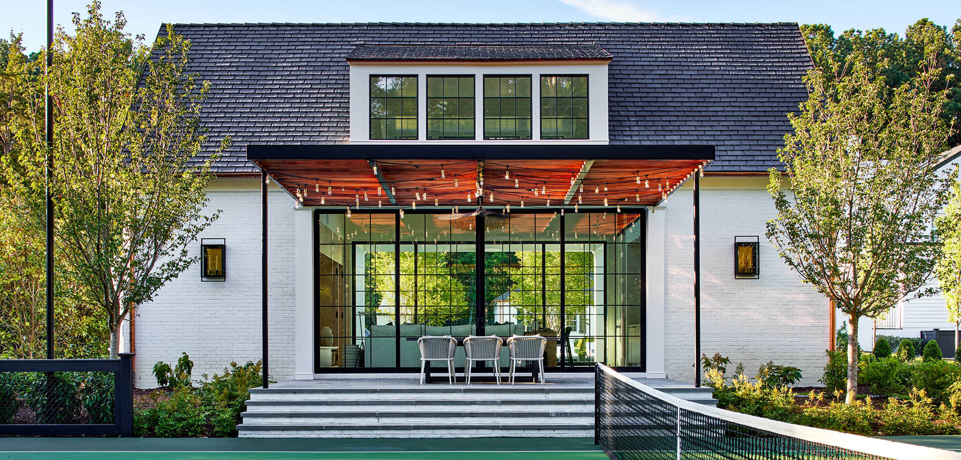The pool house entrance facing the tennis court has an open steel and wood pergola. 