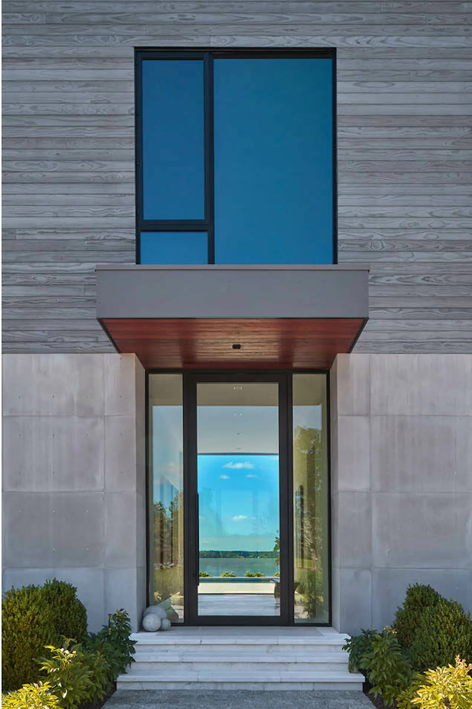 The exterior of the contemporary riverfront home shows ample glazing and neutral, natural materials. 