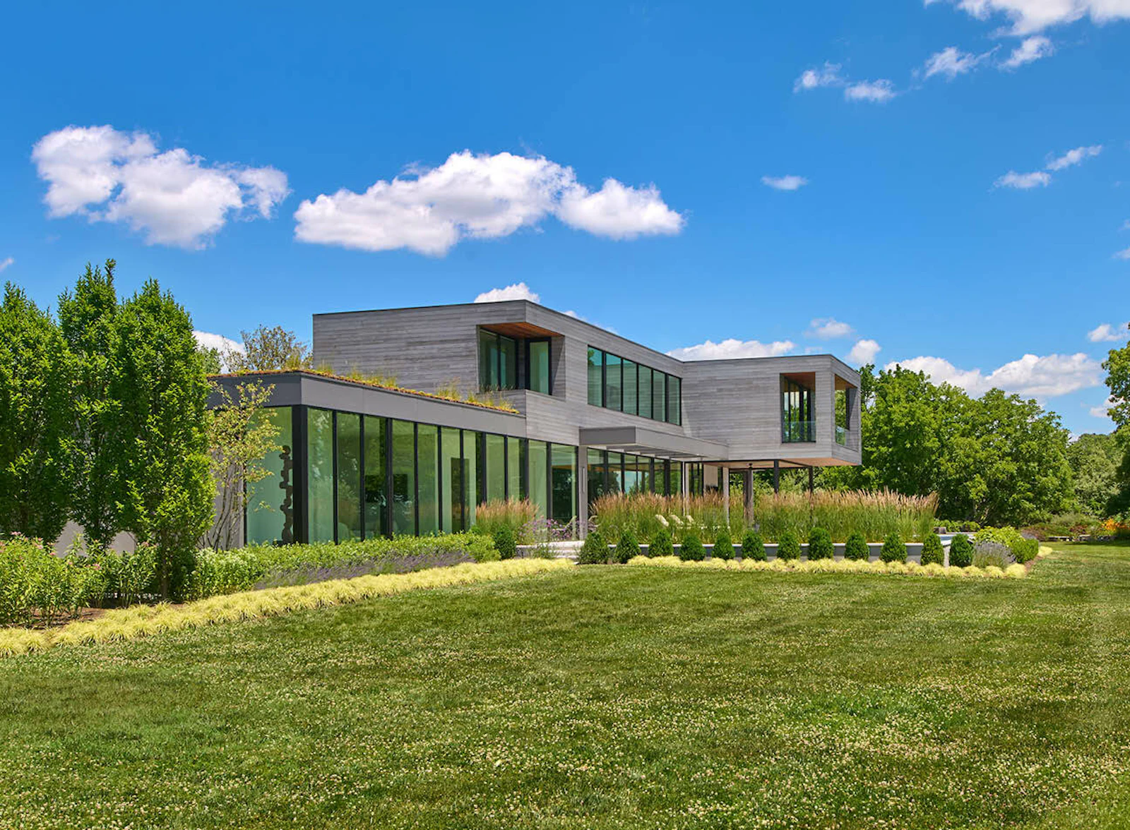 The exterior of the contemporary riverfront home shows ample glazing and neutral, natural materials. 