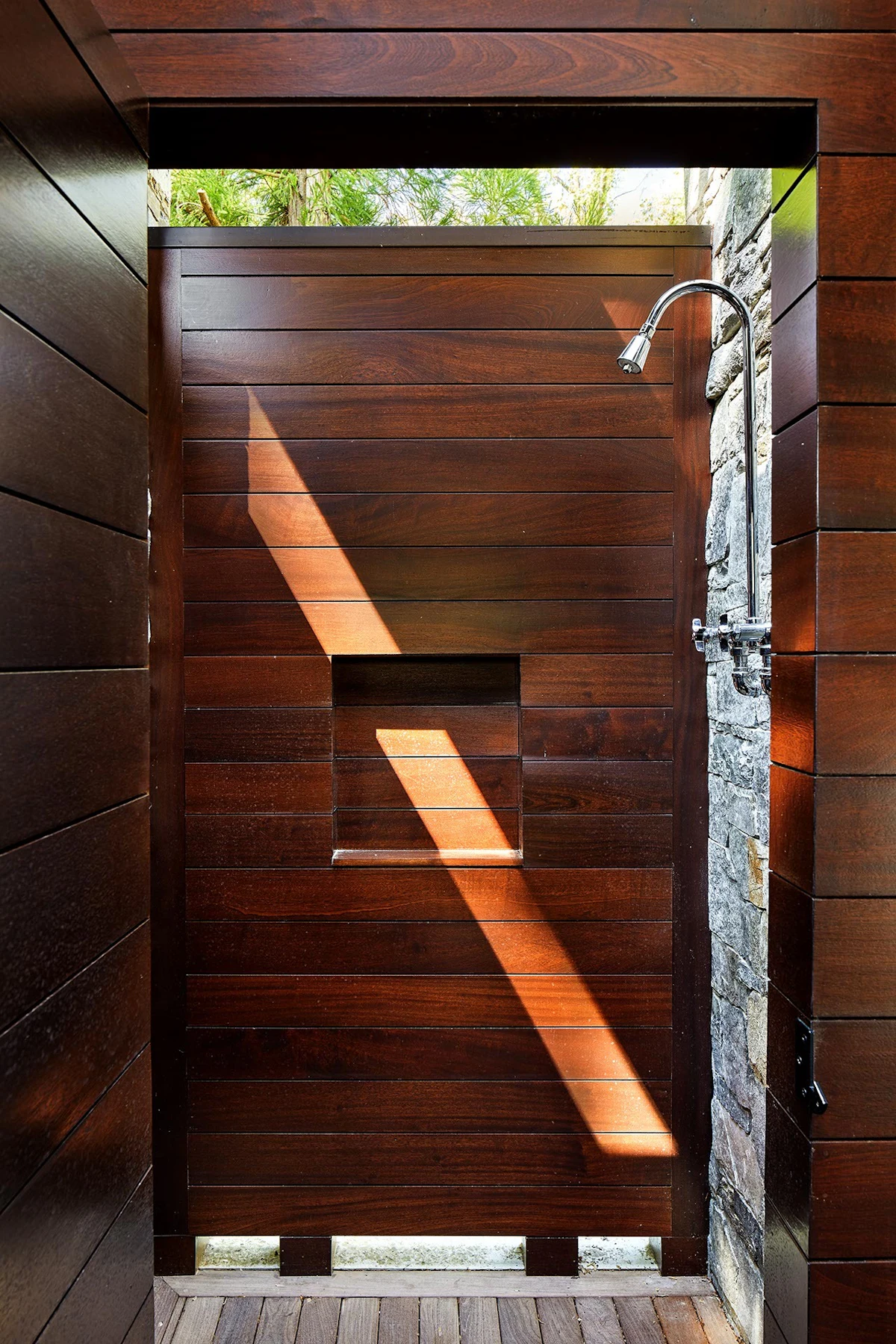 An outdoor shower features stone walls and sapele mahogany wood. 
