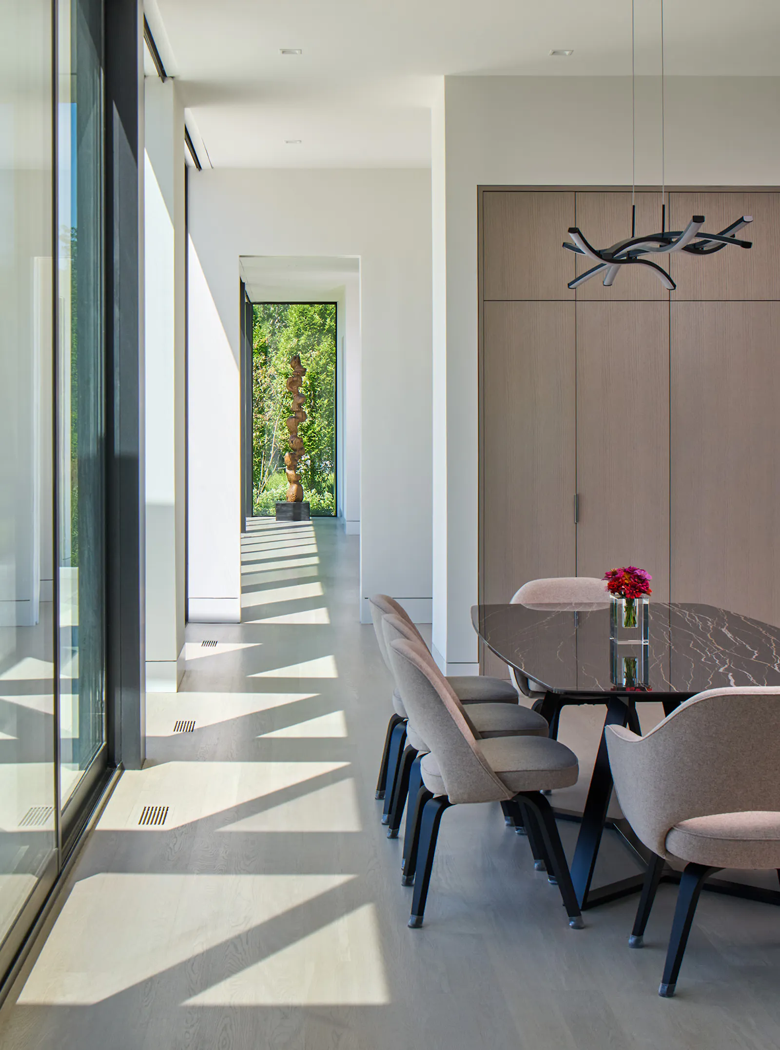 Sun shines in on a small dining area and a luxurious living space surrounding a concrete-paneled fireplace. 