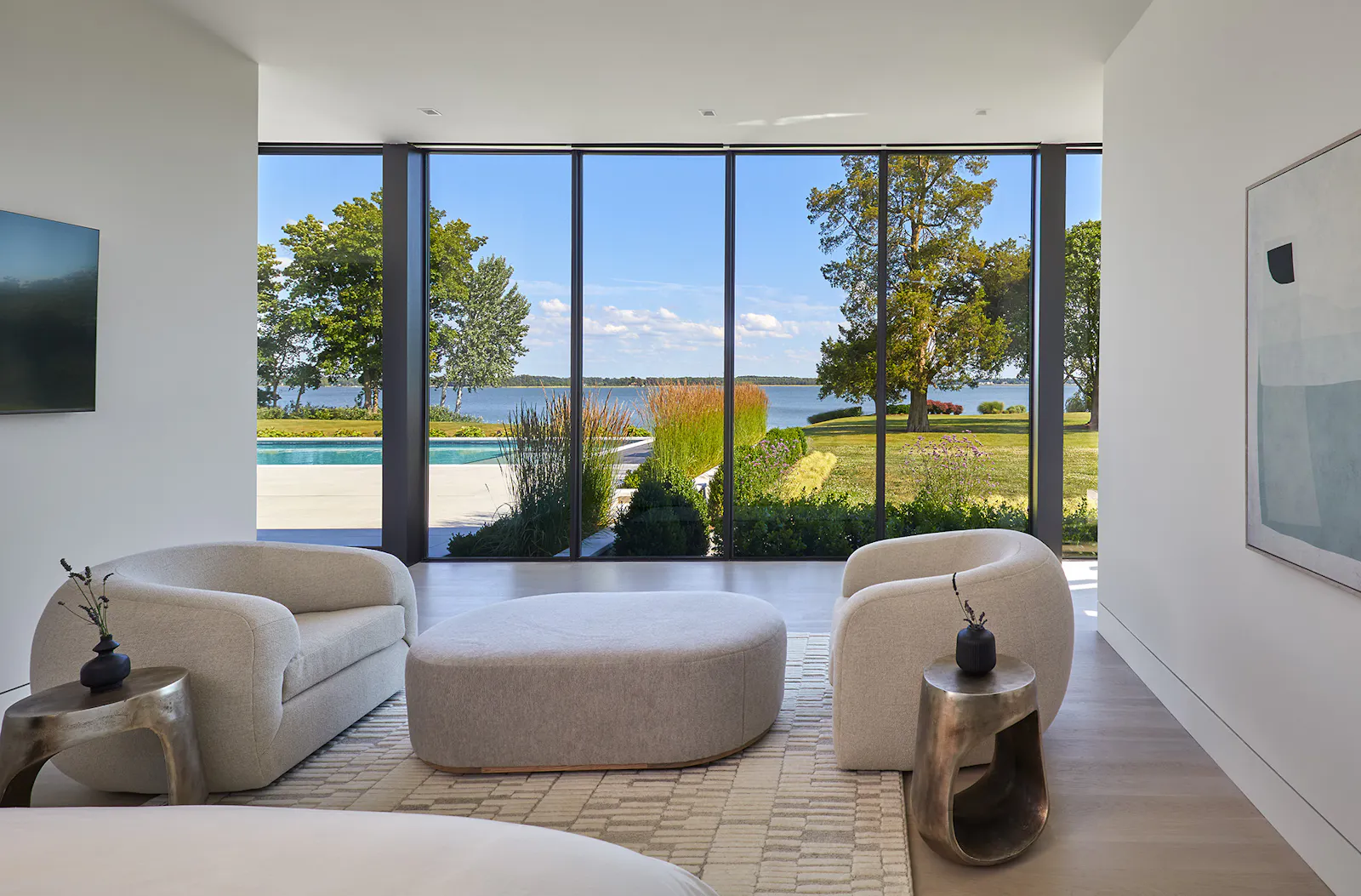 A minimal sitting room with cream-colored, modern furniture sits before a luxurious view of the pool and river. 