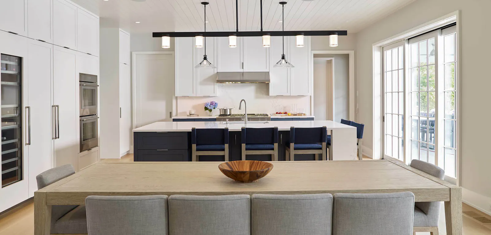 The view into the home's kitchen, including a modern dining room table and chair, a wall of white cabinetry, and hanging lights