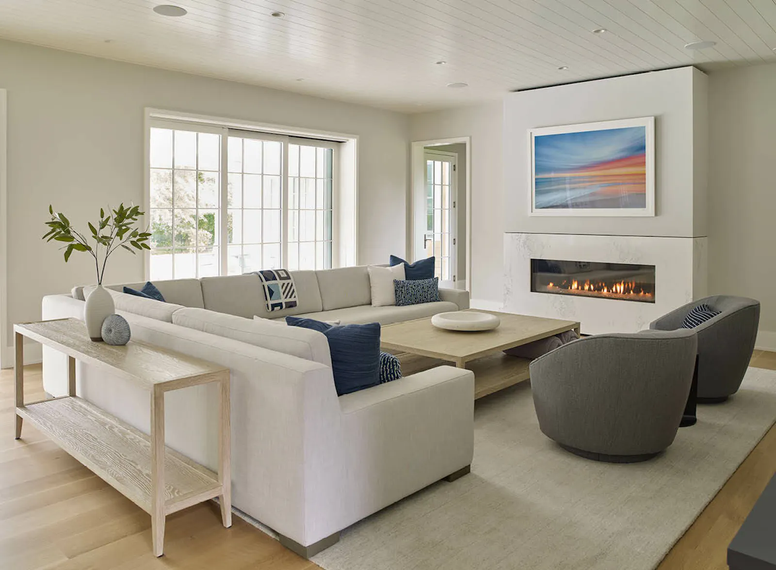 A cozy living room and kitchen include white furniture, a white fireplace, and white and blue cabinetry. 