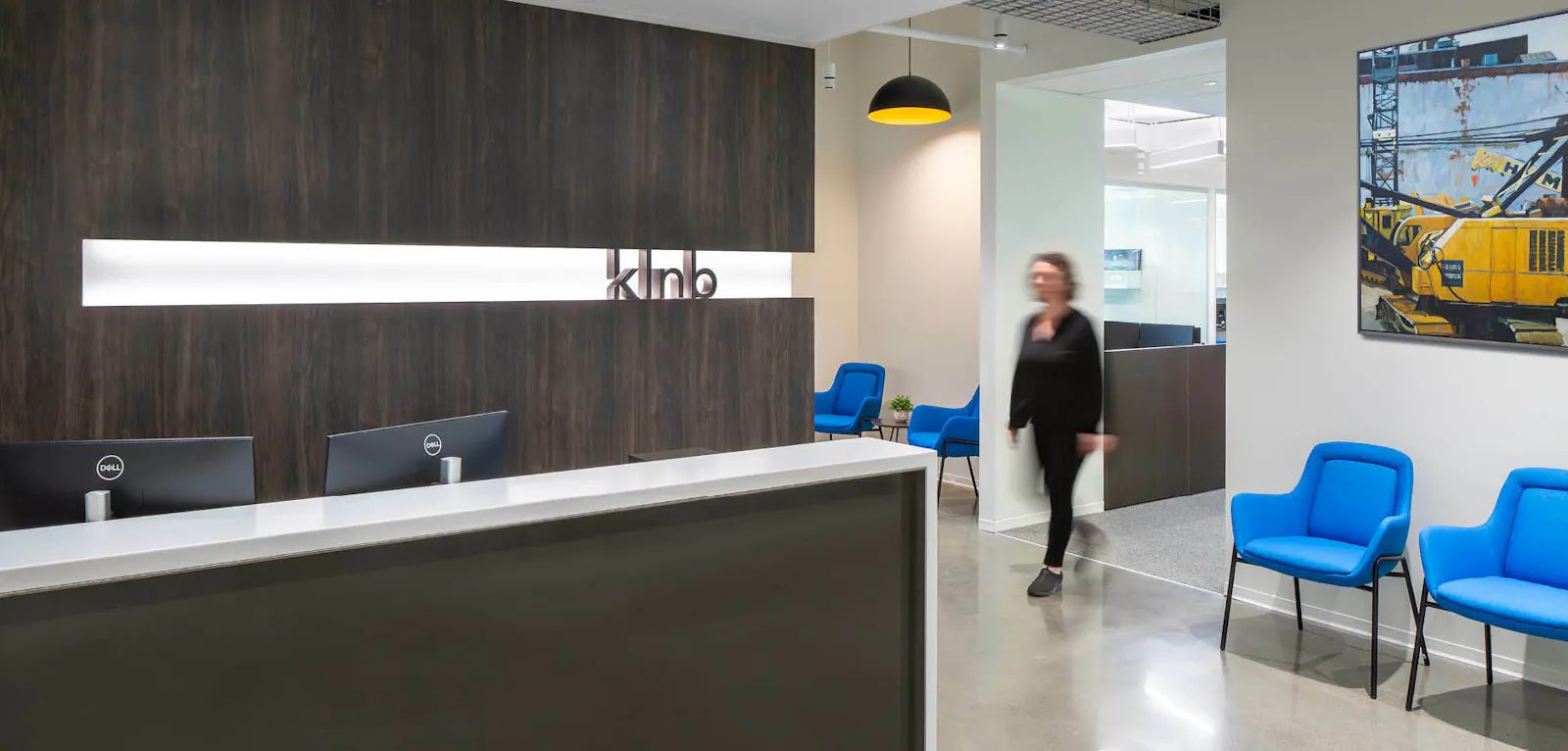 The front desk of KLNB's office featuring a wood-look statement wall and company branding surrounded by white walls and blue chairs