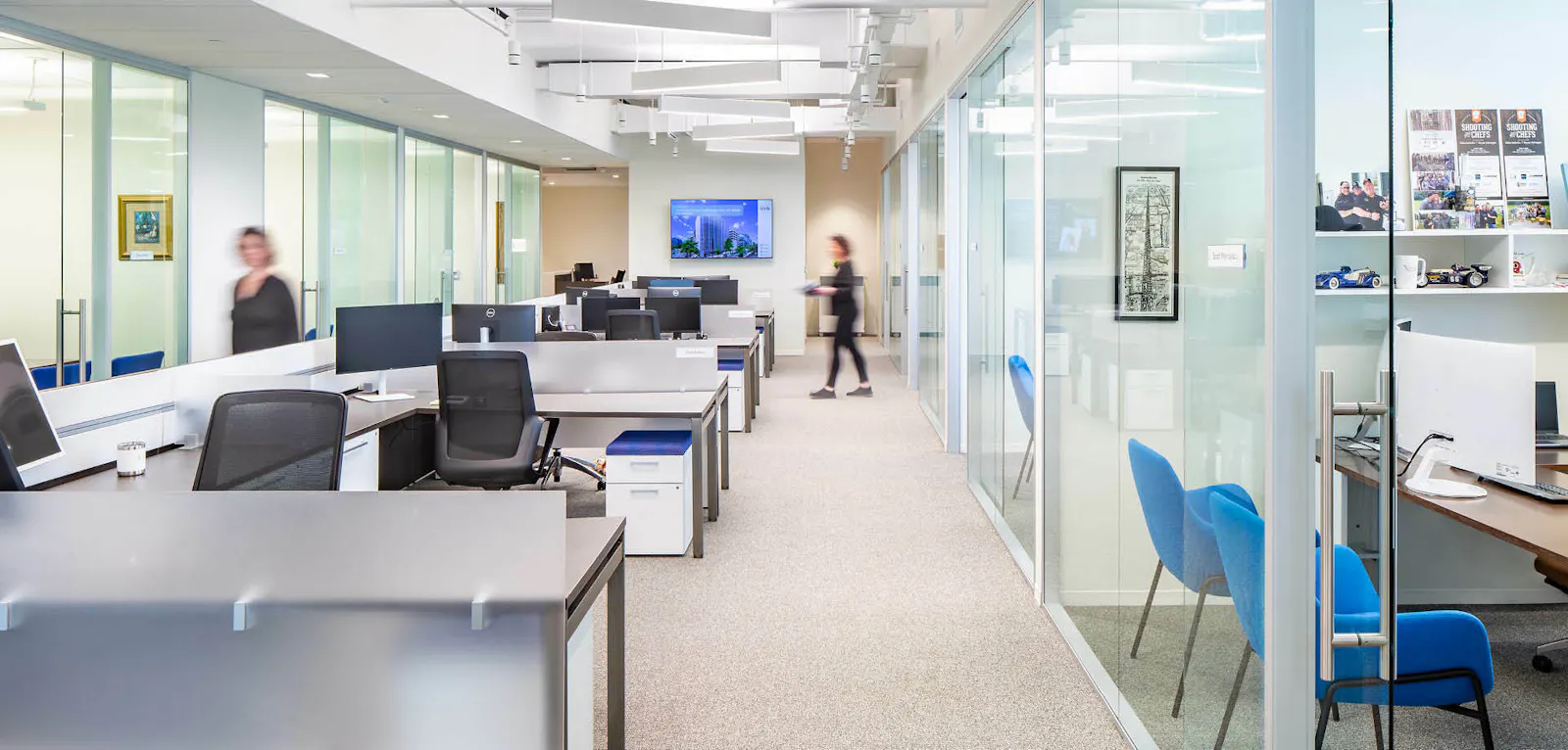 A modern workplace featuring white workstations, black chairs, and glass-front offices 