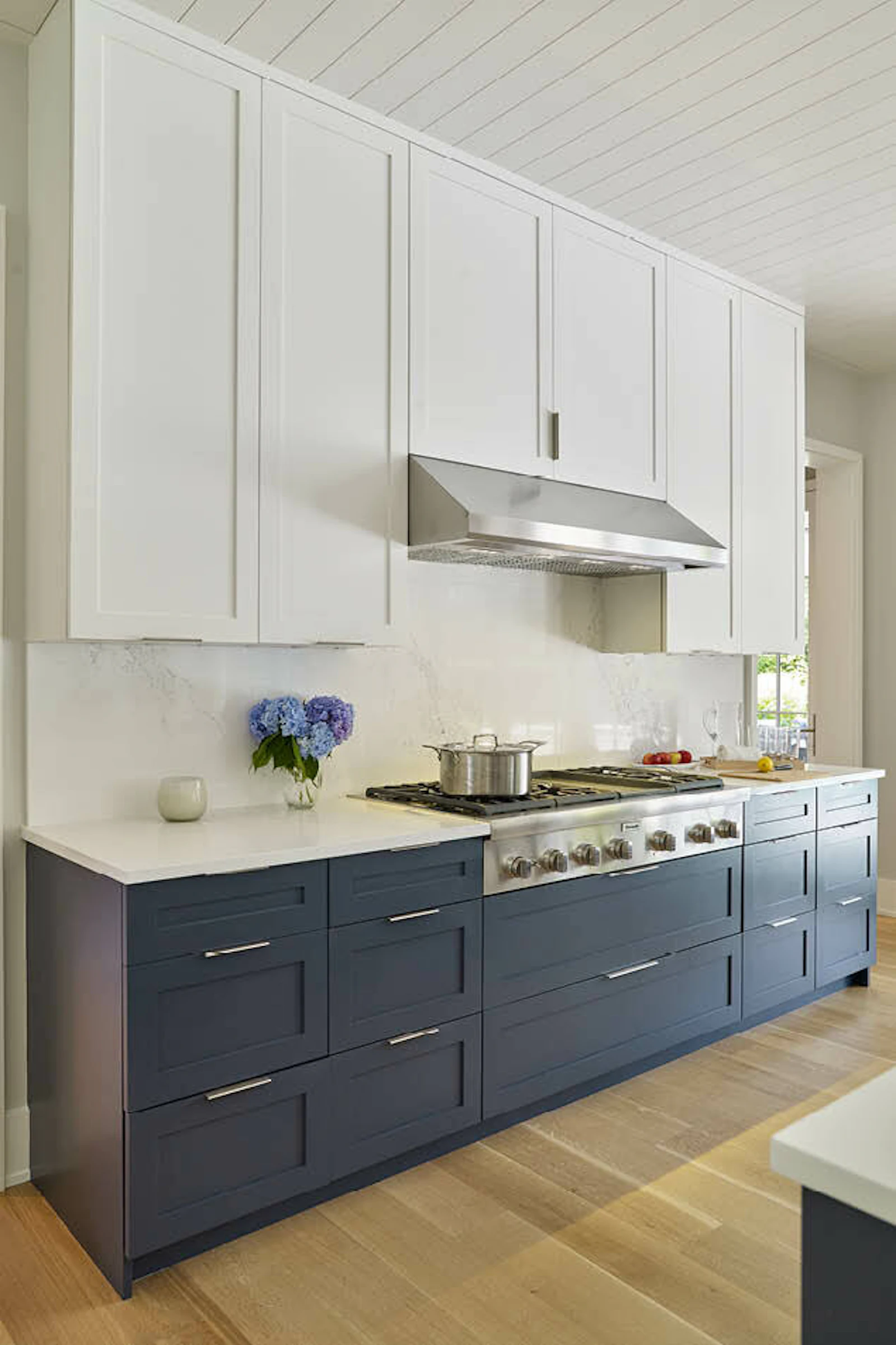 A cozy living room and kitchen include white furniture, a white fireplace, and white and blue cabinetry. 